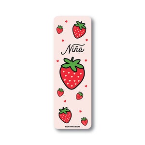Op de afbeelding: Roze bladwijzer met een aardbeienontwerp en het woord "Niña" in cursief. De bladwijzer is versierd met kleine rode hartjes.