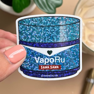 May include: A sticker featuring a blue glitter design with the words "VapoRu" and "Sana Sana". The sticker has a net weight of 1.43 oz and the Instagram handle @comadreculture.