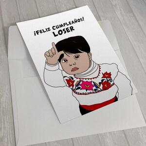 K&ouml;nnte beinhalten: Eine wei&szlig;e Gru&szlig;karte mit dem Text "&iexcl;FELIZ CUMPLEA&Ntilde;OS! LOSER" zeigt eine Cartoon-Illustration eines Kindes, das eine Verlierer-Geste macht. Das Kind tr&auml;gt ein wei&szlig;es Hemd mit bunten Blumenstickereien. Die Karte befindet sich in einem wei&szlig;en Umschlag.
