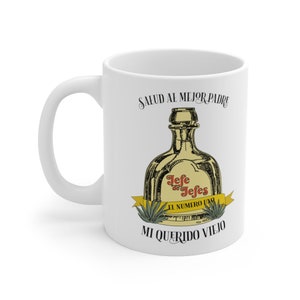 Könnte beinhalten: Weißer Keramikbecher mit Henkel. Der Becher zeigt eine Grafik einer Tequilaflasche mit den Worten "Jefe de Jefes El Numero Uno" und den Sätzen "Salud al Mejor Padre" und "Mi Querido Viejo" in Schwarz.