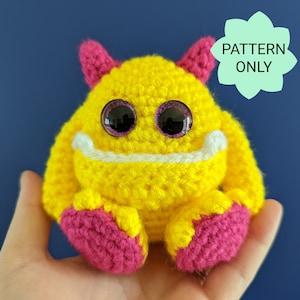 May include: A crocheted yellow monster with pink feet and purple glitter eyes. The monster has a white stitched smile. The text "PATTERN ONLY" is in a green speech bubble.