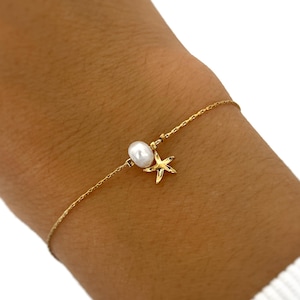 Könnte beinhalten: Ein zartes goldenes Armband mit einer kleinen, glänzenden Perle und einem Seestern-Anhänger. Das Armband ist eine feine Kette, perfekt für den täglichen Gebrauch. Die Perle hat einen Durchmesser von etwa 0,6 cm.