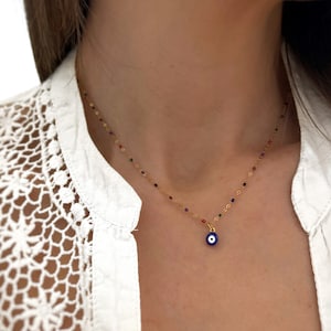 Puede incluir: Un collar de cadena dorada con un pequeño dije de ojo turco azul. La cadena está decorada con pequeñas cuentas de colores.