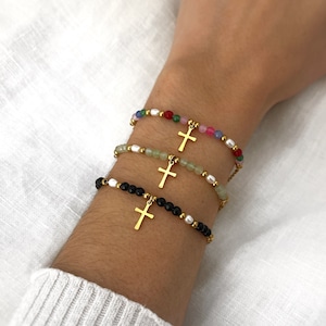 May include: Four bracelets with gold cross charms. The bracelets are made with different colored beads, including black, white, green, pink, red, and blue.