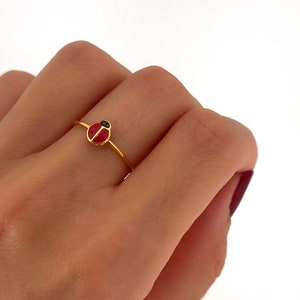 Puede incluir: Un anillo dorado con un diseño de mariquita roja con puntos negros y cabeza negra. El anillo es fino y delicado, mostrando una estética simple pero encantadora. La mariquita es el punto focal del anillo.