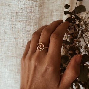 Peut inclure: Une bague en or avec un motif de vague. La bague est portée au doigt.