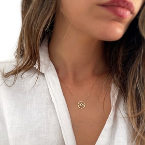 May include: A gold necklace featuring a dainty mountain pendant. The pendant is a simple outline of a mountain range within a circle.