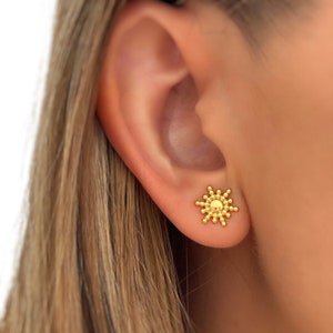 Peut inclure: Boucles d'oreilles dorées en forme de soleil avec un design texturé. Les boucles d'oreilles sont petites et délicates, parfaites pour un usage quotidien.