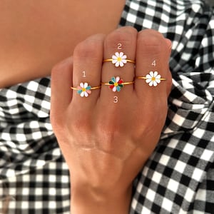 May include: Four gold daisy rings with different coloured enamel centres. The rings are numbered 1 through 4.