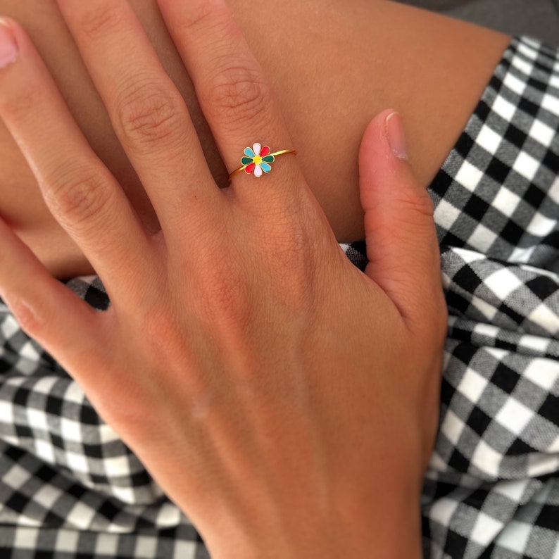 May include: A gold ring featuring a colourful enamel flower design. The flower has petals in shades of red, green, blue, white and yellow.