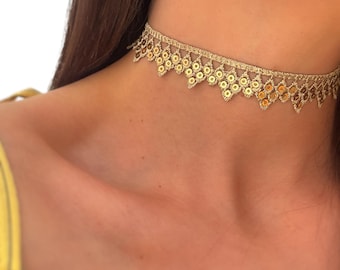 May include: A gold-colored lace choker necklace featuring a delicate woven pattern with small, circular metallic sequins integrated throughout the design, creating a scalloped edge that rests against the neck in a close-fitting, band-like style.