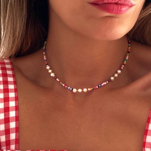 May include: A colorful beaded choker necklace with white pearl accents. The necklace is made of small, colorful beads and features a few larger white pearls.