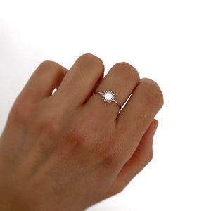 May include: A silver ring with a sun design. The ring is thin and delicate.