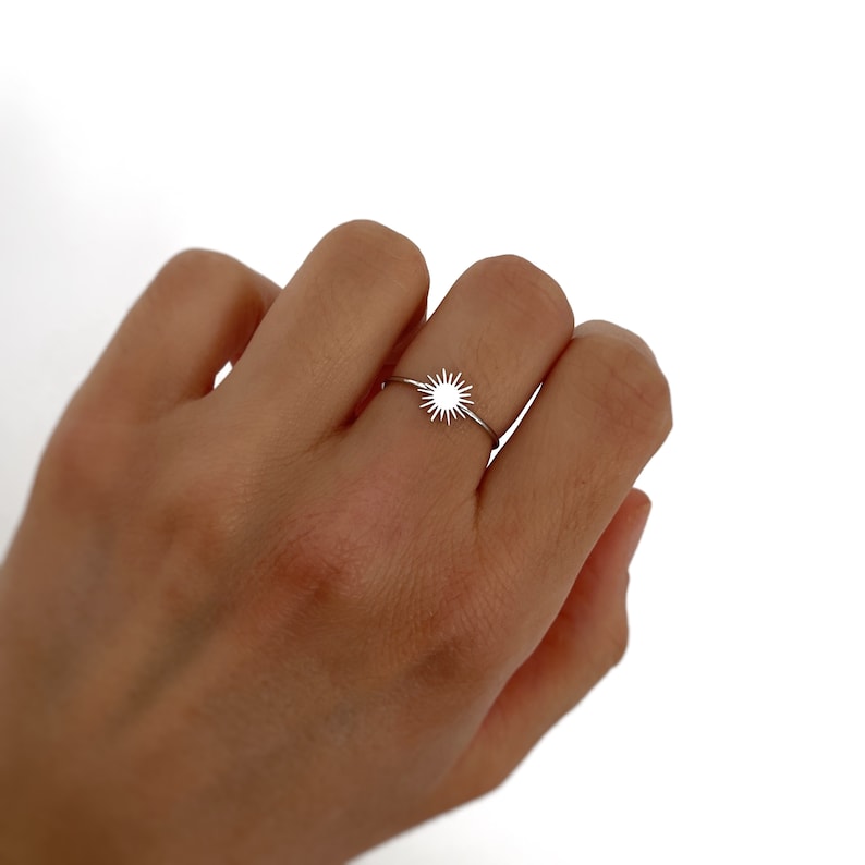 May include: A silver ring with a sun design. The ring is thin and delicate.