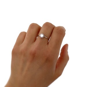 May include: A silver ring with a sun design. The ring is on a person's finger.