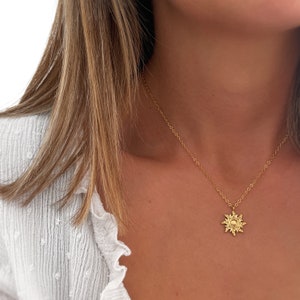 Op de afbeelding: Een gouden ketting met een zonnenhanger. De hanger is een gestileerde zon met een rond midden en stralende punten.