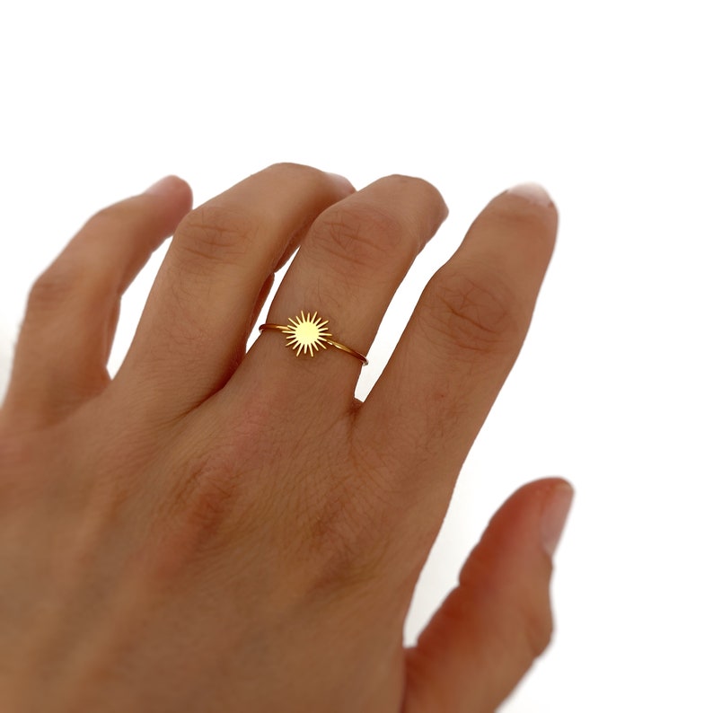 May include: A gold ring with a sun design. The ring is on a person's finger.