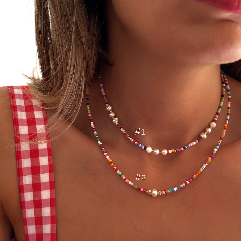 May include: Two layered necklaces with colorful beads and white pearls. The top necklace has three pearls and the bottom necklace has one pearl. The necklaces are labeled #1 and #2.
