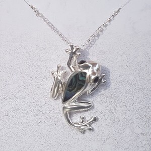 May include: Silver necklace with a frog pendant. The frog is made of silver and has a blue and green abalone shell inlay.