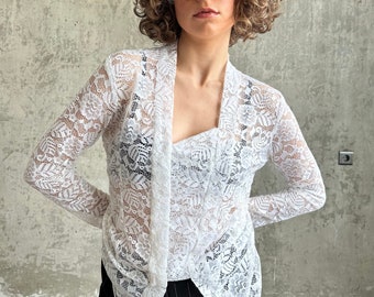 May include: White lace cardigan with long sleeves and a V-neck. The cardigan is sheer and has a delicate floral pattern.