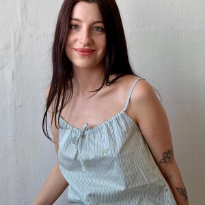 May include: Light blue and white striped pajama set. The top has thin straps and a small bow at the neckline. A small green embroidered dog is on the top. The matching pants are also striped.