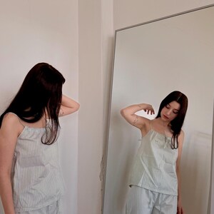 May include: A light green and white striped pajama set. The set includes a camisole top with thin straps and matching cropped pants. The person is standing in front of a mirror.