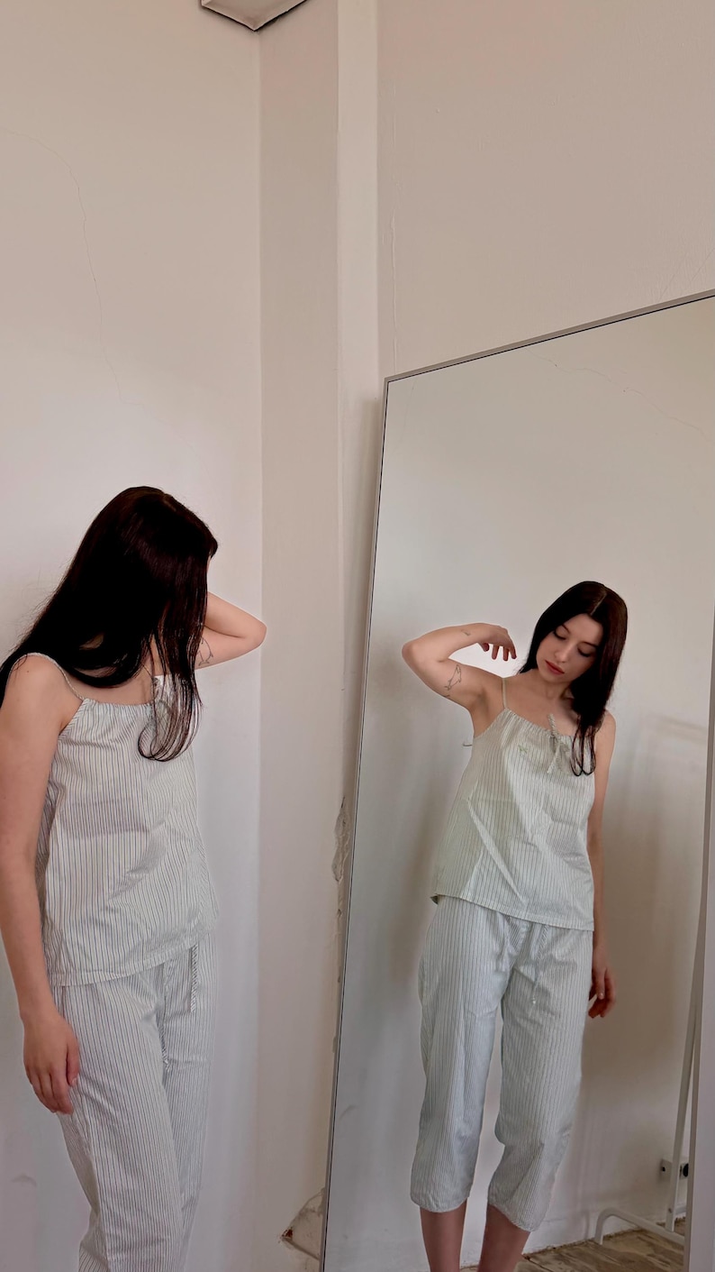 May include: A light green and white striped pajama set. The set includes a camisole top with thin straps and matching cropped pants. The person is standing in front of a mirror.