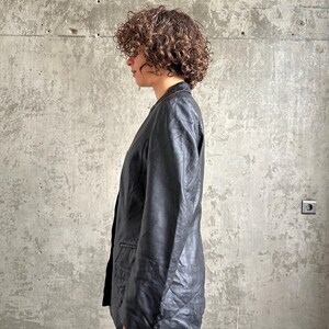 Puede incluir: Un blazer de cuero negro con un dise&ntilde;o cl&aacute;sico. El blazer presenta una solapa con muescas, un cierre de dos botones y un corte entallado. Las mangas tienen pu&ntilde;os abotonados. El blazer se usa con vaqueros azules.