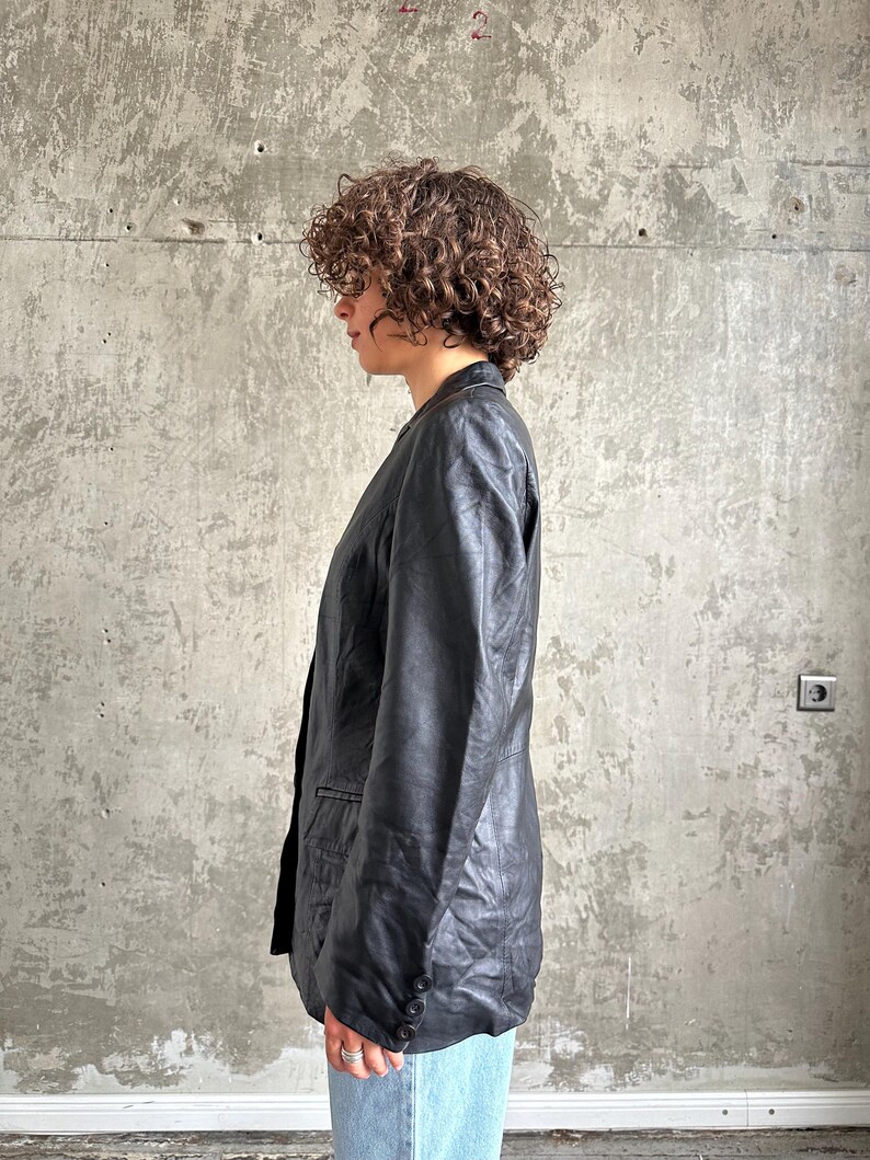 Puede incluir: Un blazer de cuero negro con un dise&ntilde;o cl&aacute;sico. El blazer presenta una solapa con muescas, un cierre de dos botones y un corte entallado. Las mangas tienen pu&ntilde;os abotonados. El blazer se usa con vaqueros azules.