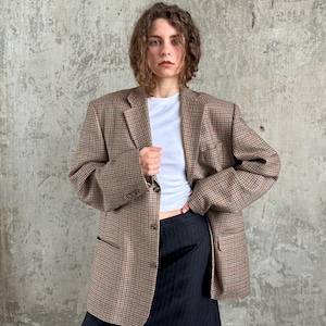 Peut inclure: Un blazer oversize à carreaux marron et beige avec un revers cranté et trois boutons sur le devant, porté sur un t-shirt blanc à col rond et une jupe noire à fines rayures. Le blazer présente des manches longues et deux poches à rabat.