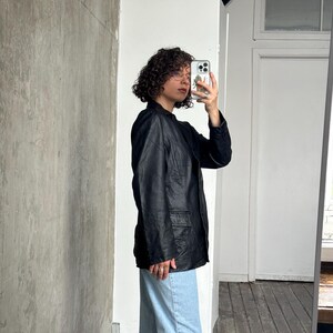 Puede incluir: Una blazer de cuero negro con dos bolsillos delanteros. La blazer se lleva con vaqueros azul claro. La persona sostiene un tel&eacute;fono frente a un espejo.
