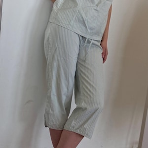May include: Light green and white striped pajama set. The set includes a camisole top with a bow detail and capri-length pants. The top has thin straps and a small embroidered detail. The pants have a drawstring waist. The model is wearing green mules.