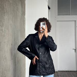 Puede incluir: Una blazer de cuero negro con un dise&ntilde;o cl&aacute;sico. La blazer tiene solapas con muescas, dos bolsillos delanteros y cierre de tres botones. Las mangas tienen pu&ntilde;os abotonados. La blazer se lleva con vaqueros azul claro.