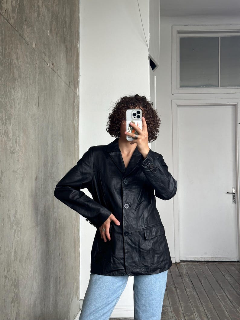 Puede incluir: Una blazer de cuero negro con un dise&ntilde;o cl&aacute;sico. La blazer tiene solapas con muescas, dos bolsillos delanteros y cierre de tres botones. Las mangas tienen pu&ntilde;os abotonados. La blazer se lleva con vaqueros azul claro.