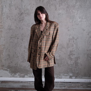 May include: A brown and tan plaid blazer with a classic check pattern. The blazer has a relaxed fit and is paired with brown pants and dark burgundy boots. The outfit is a vintage style.