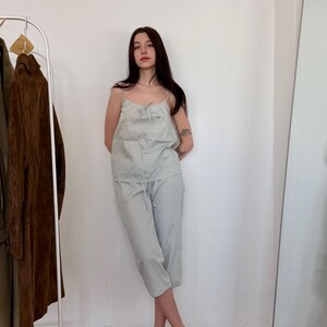 May include: A light blue and white striped pajama set. The set includes a camisole top with a bow detail and matching cropped pants. The person is wearing green patterned shoes. A clothing rack and mirror are in the background.