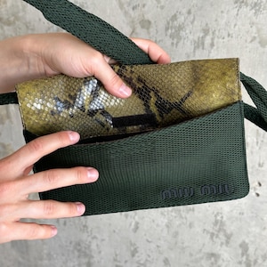Può includere: Una borsa a tracolla in rete verde scuro con una patta caratterizzata da un motivo a pelle di serpente giallo e nero. La borsa include una tracolla in tessuto verde scuro abbinata e la scritta miu miu impressa in verde scuro in basso a destra.