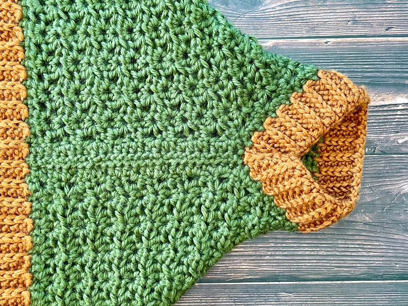 Close up of the sleeve of a dark green textured crochet shrug with gold folded over ribbed collar and cuff.