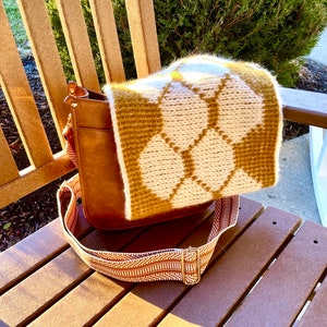 Cream Tunisian Crochet cowl with gold honeycomb motif draped over brown leather bag, sitting on a lawn chair in the sunshine.