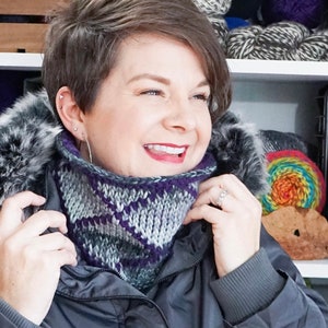 Grey and Purple reversible Tunisian Crochet Cowl modelled on smiling dark haired woman with Parka jacket.