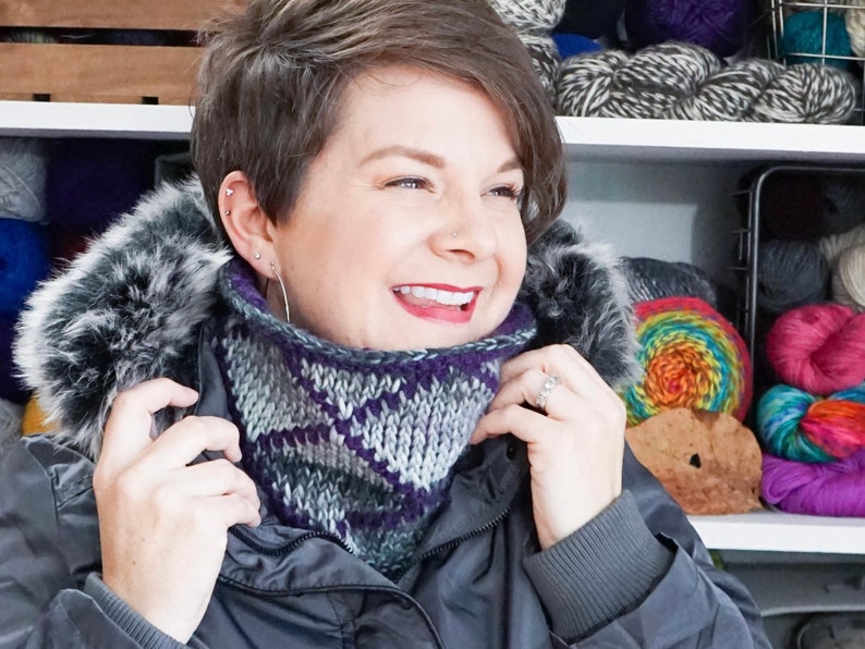 Grey and Purple reversible Tunisian Crochet Cowl modelled on smiling dark haired woman with Parka jacket.