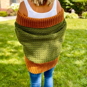 Dark green textured crochet shrug with gold folded over ribbed collar and cuffs, modelled on blond woman wearing white tank top and blue denim jeans, viewed from the back.