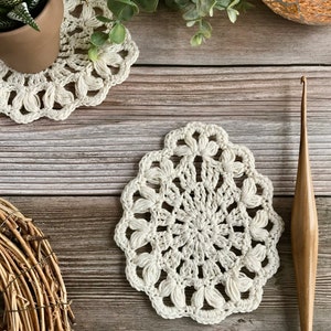 May include: Two white crocheted doilies on a wooden surface. A wooden crochet hook is also on the surface.