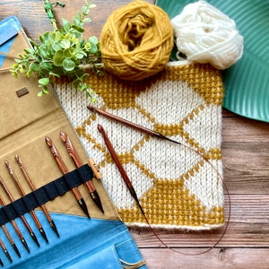Cream and gold hexagon crochet cowl on table, with remains of gold and cream yarn balls, and a folding case of Tunisian Crochet hooks