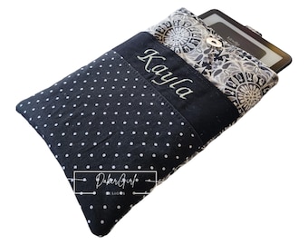 May include: A black fabric sleeve with white polka dots and a gray patterned top flap featuring a silver snap button. The name Kayla is embroidered in white script. A black e-reader is partially inserted. A logo reads Paper Girl Designs.