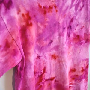 May include: A tie-dye t-shirt in shades of pink and red. The shirt has a crew neck and short sleeves. The tie-dye pattern is swirled and blended, creating a unique and colorful design.