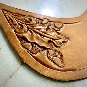 Könnte beinhalten: Nahaufnahme eines braunen Lederstücks mit einem aufwendig geschnitzten Design aus Eichenblatt und Eicheln.