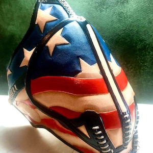 Pode incluir: Uma máscara de couro com um design de bandeira americana vermelha, branca e azul. A máscara é feita de couro e tem uma borda preta e branca. A máscara é um acessório único e elegante.