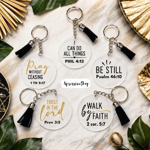 May include: Five circular clear acrylic keychains with silver metal rings and black tassels. Each features black or gold text with Bible verses: Pray Without Ceasing, I Can Do All Things, Be Still, Trust In The Lord, and Walk By Faith.