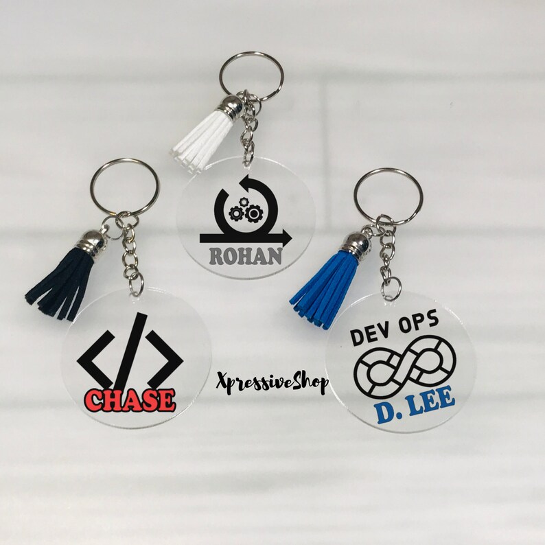 May include: clear acrylic keychains. The keychain on the left has a black tassel and a black and white code symbol </>. The keychain in the center has a white tassel and a black design of a circle with gears and an arrow. The keychain on the right has a blue tassel and a black design of an infinity symbol with the text 'DEV OPS' above. Computer Programmer Keychain Gift, Software Engineer Gift, Programming, Coder Gift, HTML CSS JavaScript Coding Keychain, Computer Science